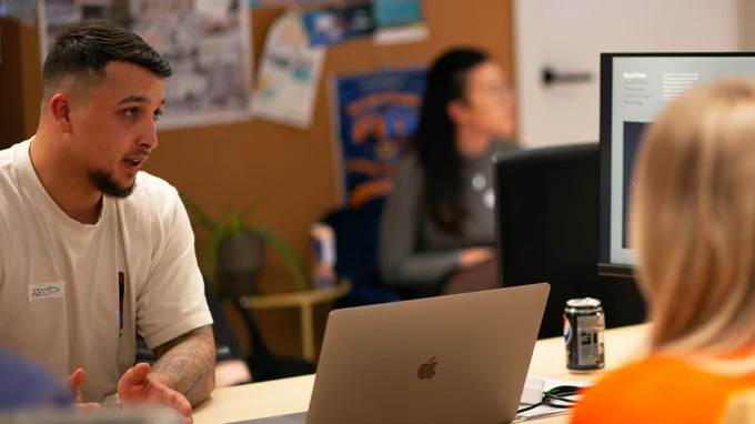 Alex, another one of our portfolio reviewers, sat at a desk with a laptop. He’s talking to and giving feedback to a group of attendees. His name tag has his nickname, Arod, on it.