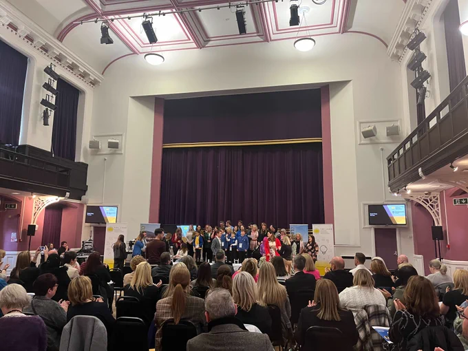 a crowd of intrapreneurs stand on stage in Alloa Town Hall. An audience looks on.