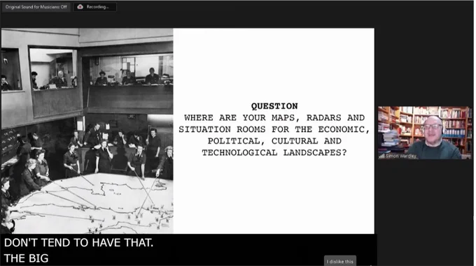 A man presenting a slide that says "Q: Where are your maps, radars and situation rooms for the economic, political, cultural and technological landscapes?"