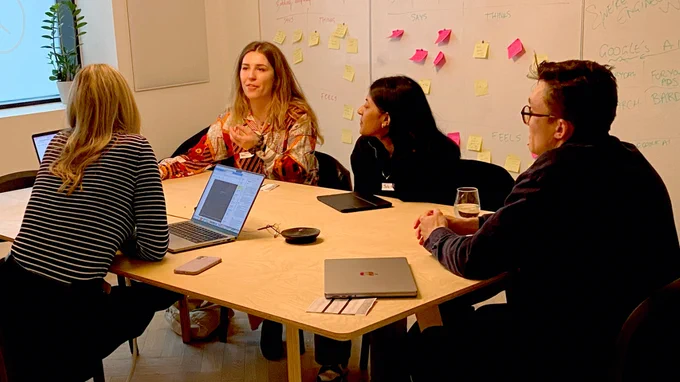 Our portfolio reviewer Hannah, and three attendees, sat in a spacious meeting room. Hannah has a laptop open in front of her and is reviewing a portfolio and having a discussion with the attendees. 