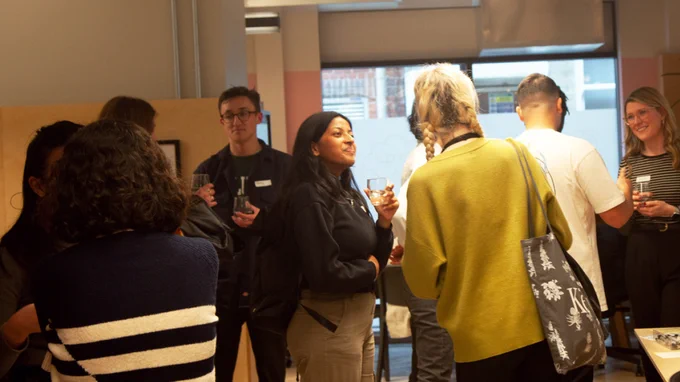 Our attendees standing in our studio holding drinks and snacks and chatting with one another. 