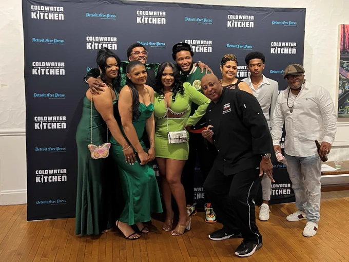 A group of people at a film festival opening reception posing in front of a screen that says Coldwater Kitchen and Detroit Free Press. 