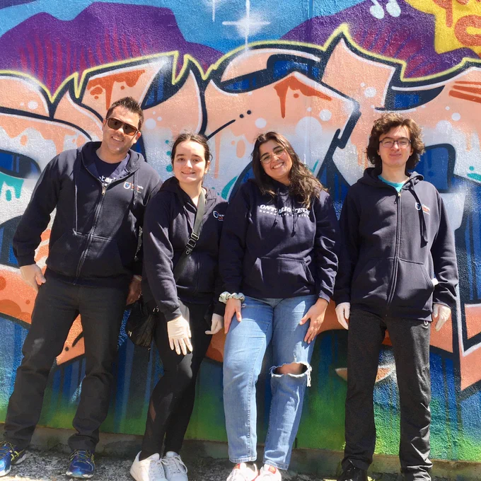 Dan and three students stand in front of a colourfully spray painted wall as they take part in the community clean up
