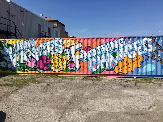 A large shipping container shows spray-painted artwork across it that reads nothing changes if nothing changes.