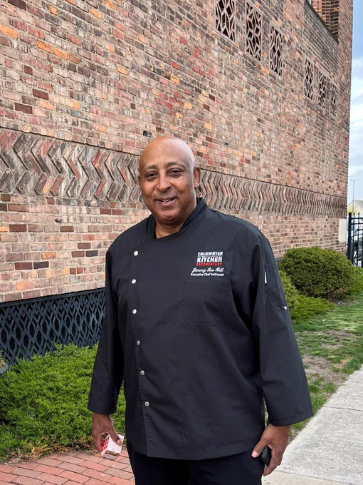 Chef Jimmy Lee Hill in a black chef unifrom standing outside the brick exterior of the Scarab Club in Detroit 