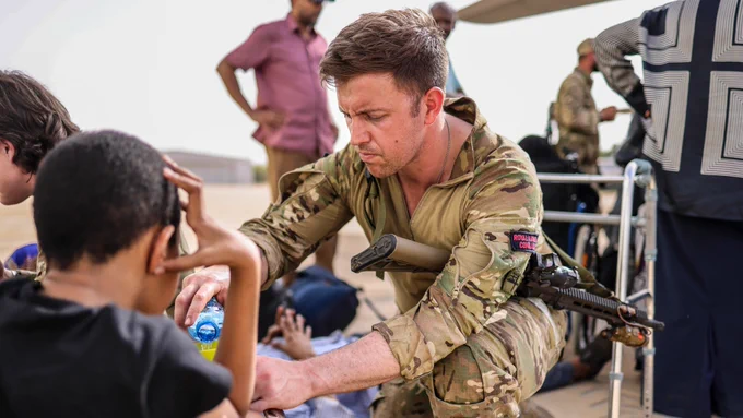 A Royal Marine looks after an evacuee whilst waiting at Wadi Seidna airport in Sudan for an aircraft bound for Cyprus. 
