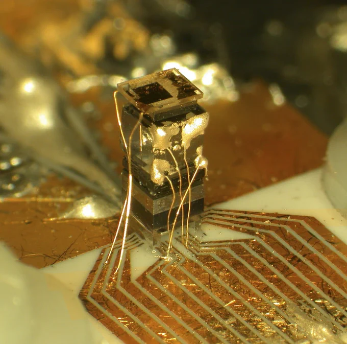 Metallic gold box with wiring attached to a gold design on the surface below.