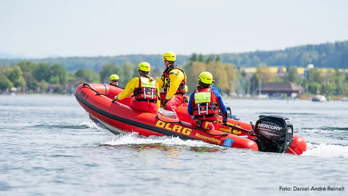 Drei DLRG Rettungsschwimmer sitzen in einem Schlauchboot und fahren übers Wasser.