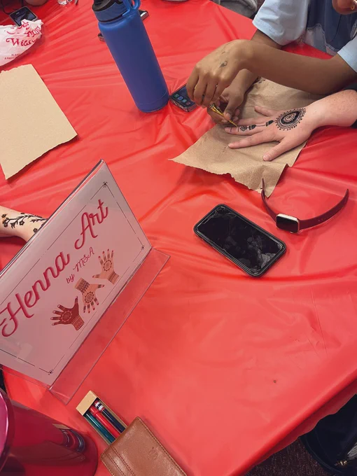 A sign displaying Henna Art by MSA, and a student giving henna art to a teacher