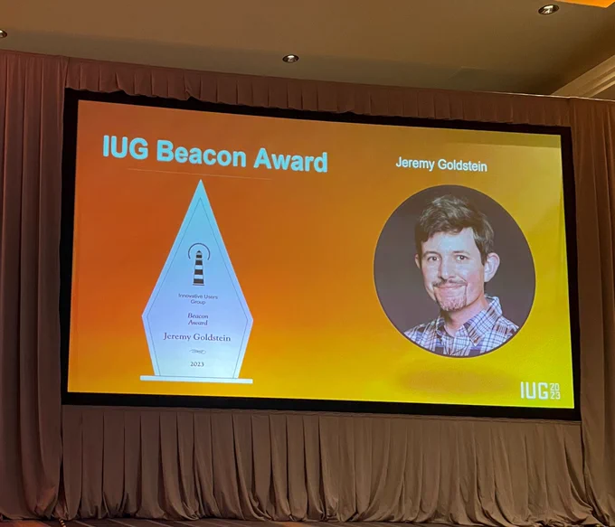 Photo of a screen showing a slide with the IUG Beacon Award and a picture of Jeremy Goldstein