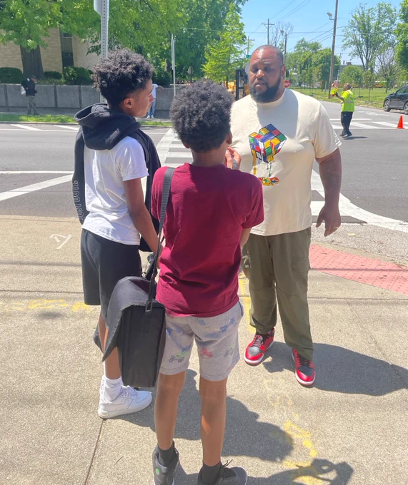Students talk to an adult on a sidewalk.