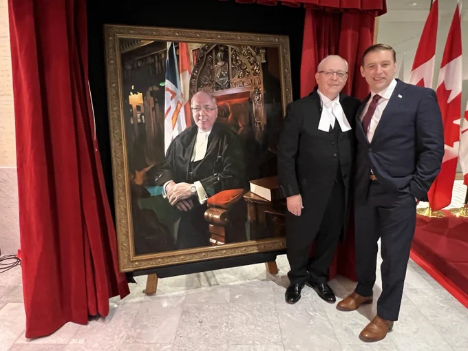 Senator and Premier stand next to the Senator's portrait. 