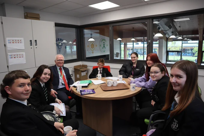 Mr Powell enjoying hot chocolate with students. They are all sat around a round table, smiling, and holding cups of steaming hot chocolate.