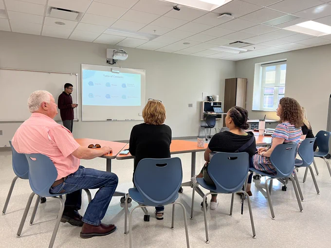 A panel of teachers and parents/guardians listen to a students’ defense of learning.