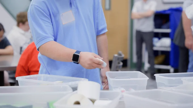 A person in a light blue collared shirt with a bue wristwatch sorting medications into their appropriate bins.