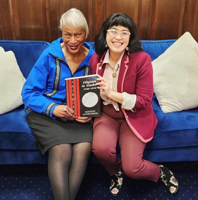 Senator Elvi Gray-Jackson and Representative Genevieve Mina holding the book “Filipinos in Alaska” and smiling.