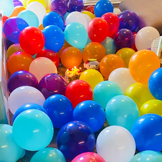 Wumpus is sitting in a room with multi colored balloons and a birthday cake in the center. 