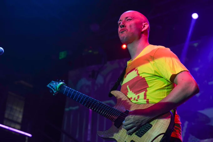 A photo of Danimal Cannon mid-stank face. He's partially lit by stage lights and is playing his lefty 7 string guitar.