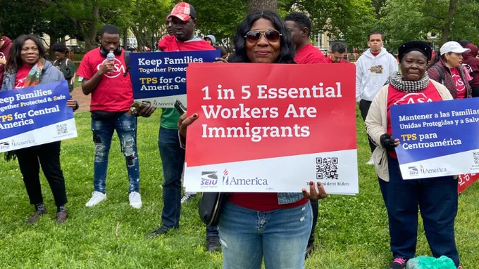 A photo of people at an outdoor rally holding picket signs. 