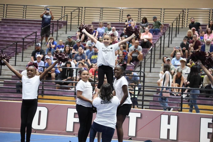 Image of cheerleaders stunting with one cheerleader in the air with her pom poms raised