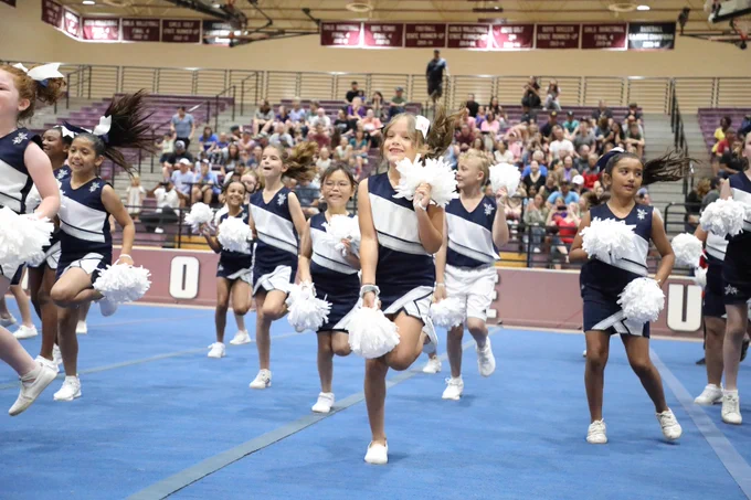 Image of cheerleaders smiling with one leg up and the other on the ground