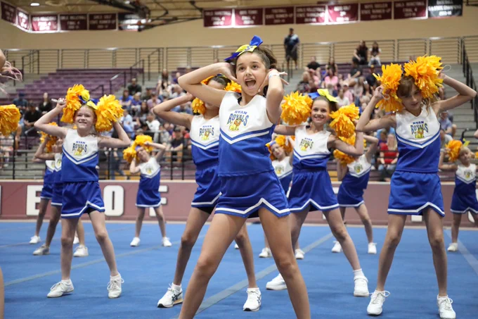 Image of cheerleader with expressive look on her face with cheerleaders behind her with pom poms near their faces