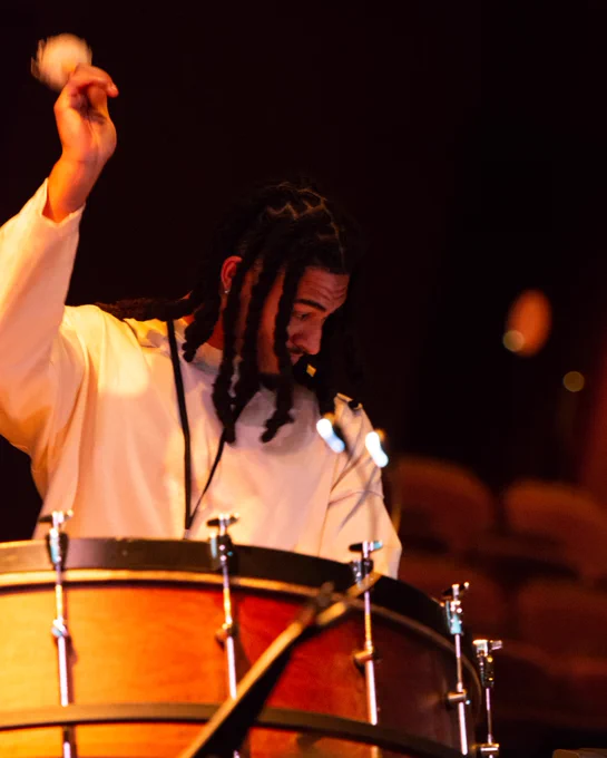 A drummer during rehearsal at Brighton Dome. Their arm is raised as they are about to hit the drum.