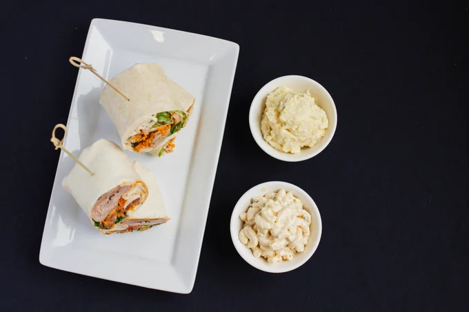 Two wraps on a plate next to macaroni and potato salad. 