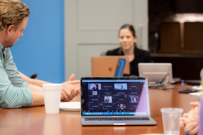 A laptop shows a Zoom gallery of online attendees.
