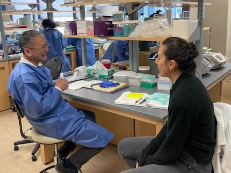 Two researchers discuss laboratory procedures by a lab bench