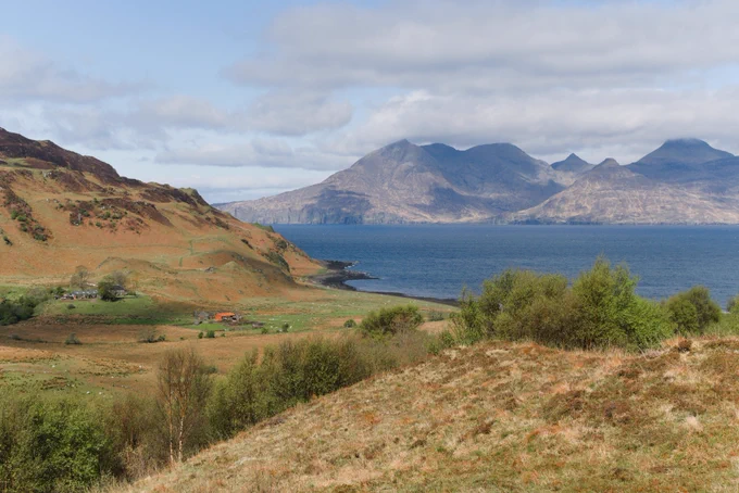Fields and hill leading down to the sea with a mountainous island in the distance