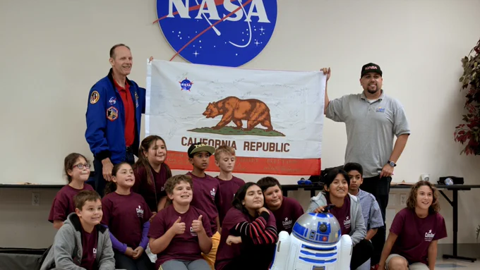 Group of students posing in front of the California State Flag and a NASA sign 