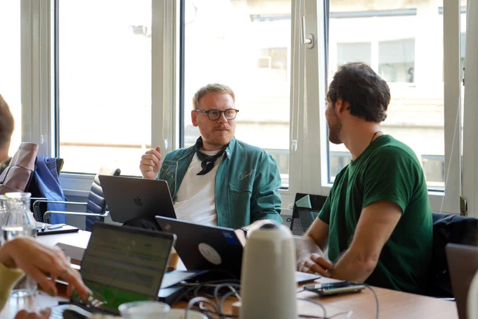 Zwei Teammitglieder diskutieren während des Meetings. Vor ihnen stehen ihre Laptops.