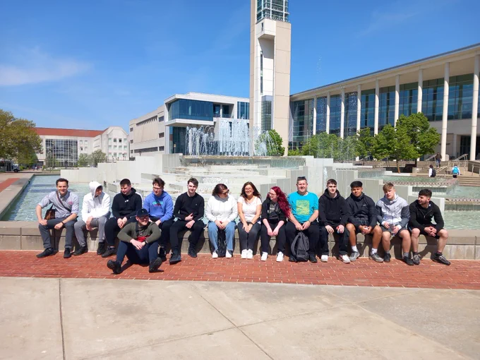 14 students posing for a photo in front of a fountain on a sunny day at Missouri State University.