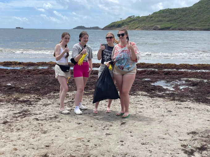 Four students posing for a photo on the beach. One of them is holding a black bin bag full of picked up litter.