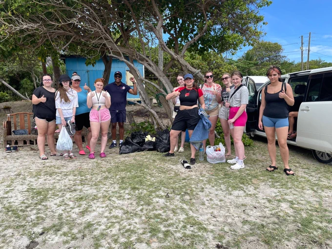 Students posing for a photo. There is a tree behind them and a clear blue sky. There are 11 people in the photo.