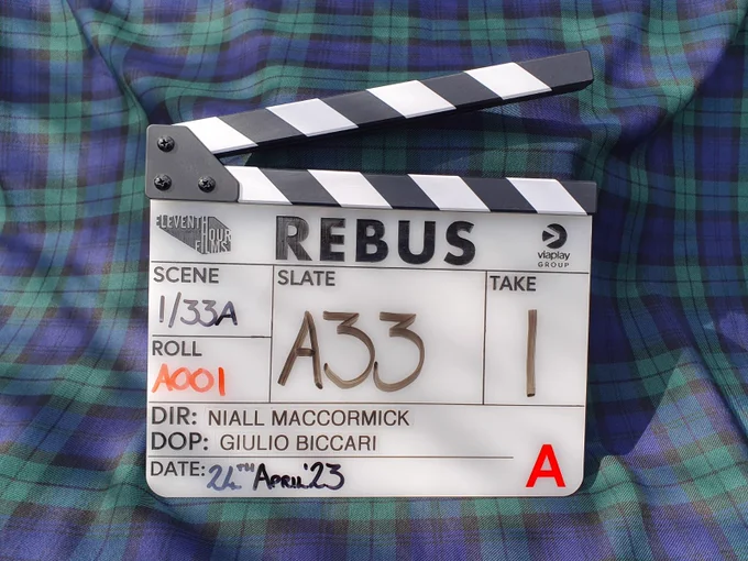 Rebus clapper board lying on top of blue and green tartan fabric