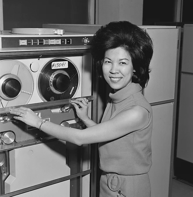 Portrait of Josephine Jue smiling as she poses with one of NASA Johnson Space Center's mainframe computers.