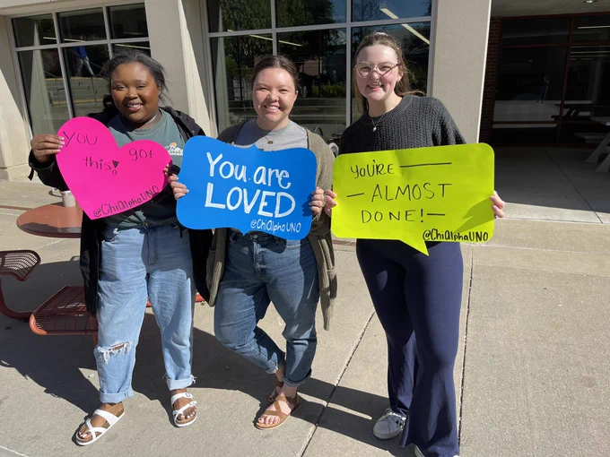 Three members of chi alpha hold up you are loved signs.