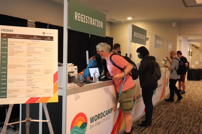 Person in pink shirt standing at WordCamp US 2022 registration table Photo Credit: Courtney Robertson