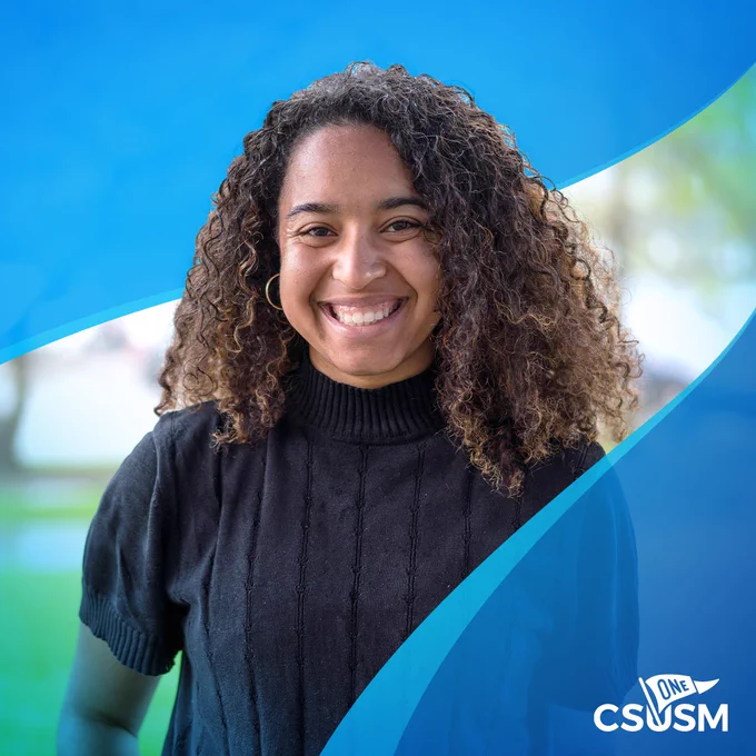 Student with curly hair and black shirt, smiling at the camera
