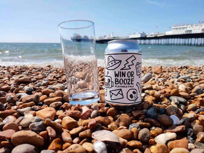 A can of loading beer and a glass sit on some rocks by the sea
