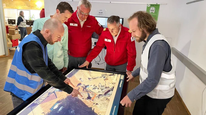 Fünf Männer der Rettungskräfte beugen sich über einen Tisch mit einem großen Screen, auf dem ein Lagebild zu erkennen ist. 

Bild: Rotes Kreuz Salzburg