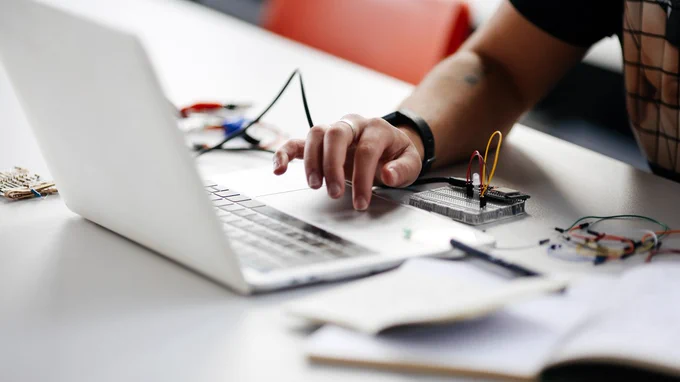 one arm in shot clicking on a laptop, with various electronic devices alongside