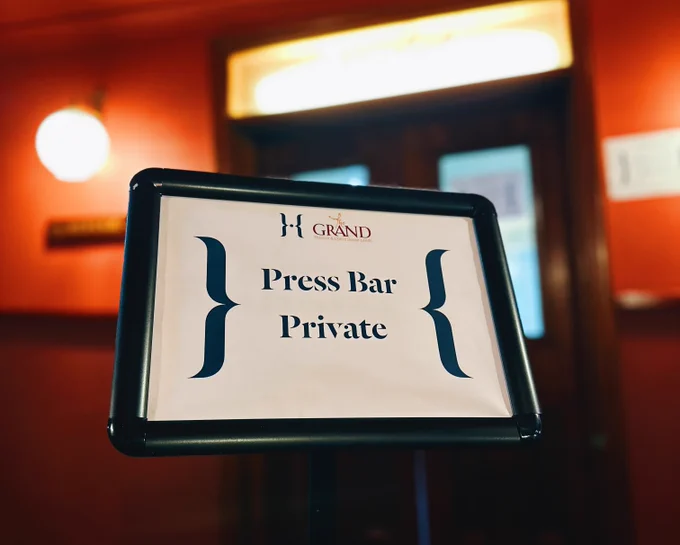 In front of a doorway illuminated by surrounding lights, a sign reads 'Press Bar: Private'.