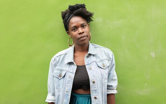 The poet Vanessa Kisuule standing against a bright green background. Photo by Jon Aitken.