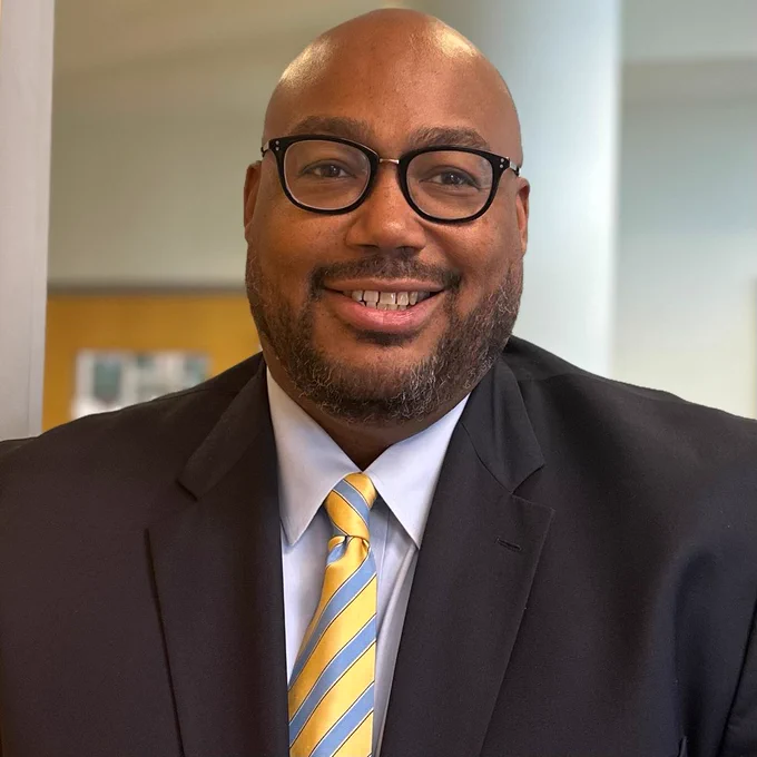 A headshot of Kevin Dashawn Anderson, wearing a suit and tie and glasses