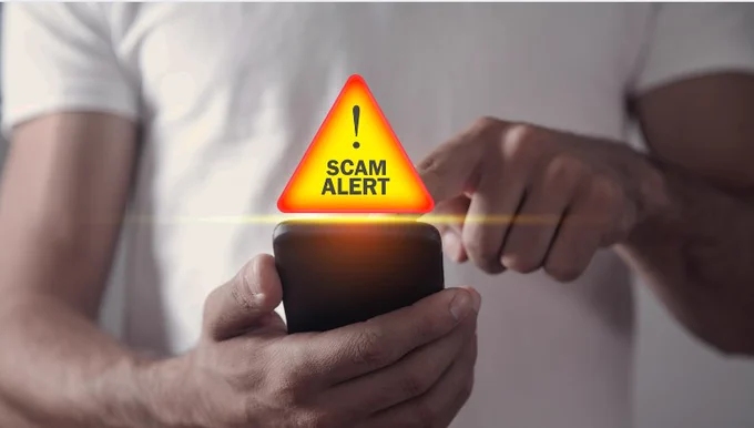 Photo of someone using a mobile phone with a graphic above it saying Scam Alert