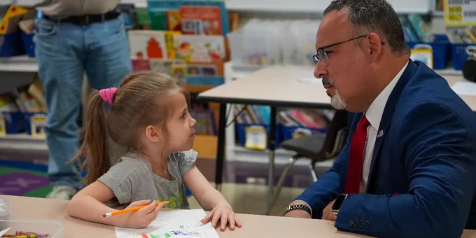 Secretary Cardona visits with a small child during a classroom visit. 