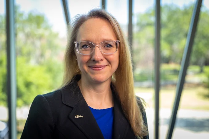 A portrait of Kristy Elizabeth Boyer standing in a building on the University of Florida campus with trees in the background.